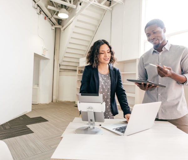 Two people talking in an office, working on tablets and a laptop