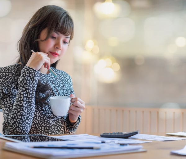 Woman drinking coffee while reading spreadsheets with a calculator