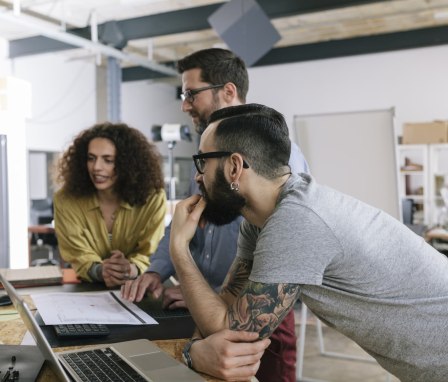 Three people working on a laptop in an office