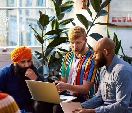 Three people talking and looking at a laptop