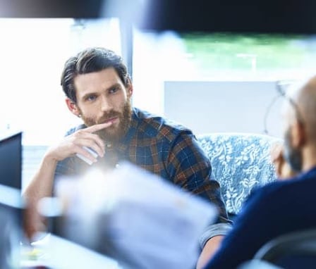 Two men talking while sitting at computer desks