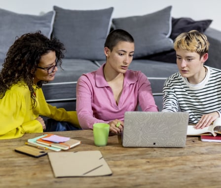 Three people working together on a laptop on a coffee table