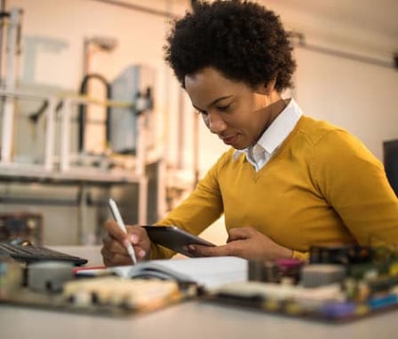 Person writing in notebook in front of desktop computer