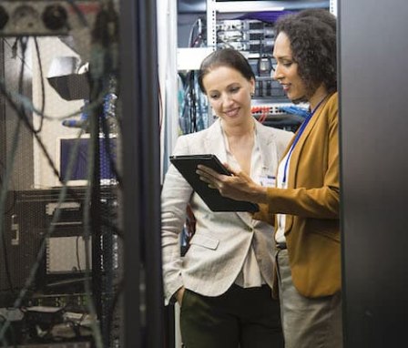 Two women working on a tablet surrounded by computer hardware