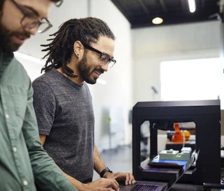 Two male colleagues talking beside 3D printer