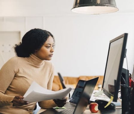 Woman holding papers and looking at computer