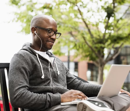 Man on park bench using laptop and ear phones