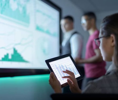 Woman using tablet to display charts on a screen to colleagues