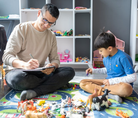 Child psychologist playing with young child on toy mat