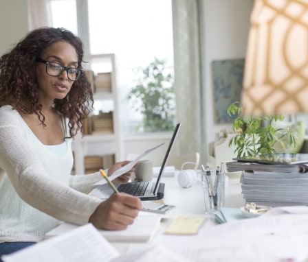 Woman writing in notebook, looking at laptop and calculator