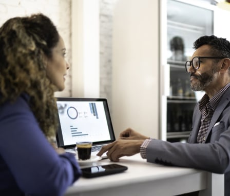 Two professionals talking beside laptop with graphs on the screen