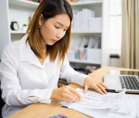 Woman looking at piece of paper with numbers on it at a computer desk