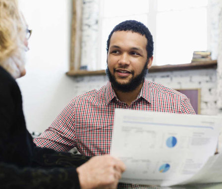 Two men talking in office about a paper with charts on it