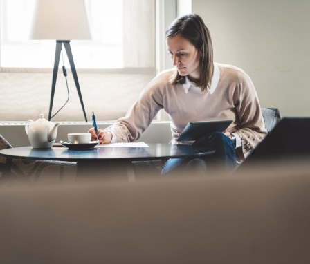 Woman writing and holding tablet beside lamp