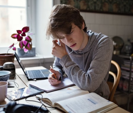 Person studying a book and writing in a notebook while sitting at a desk