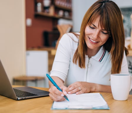 Woman writing in a notebook beside a laptop