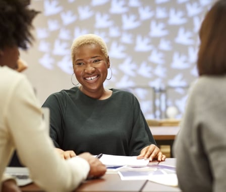 Person smiling at two others in a meeting, with papers laid out on the table in front of them