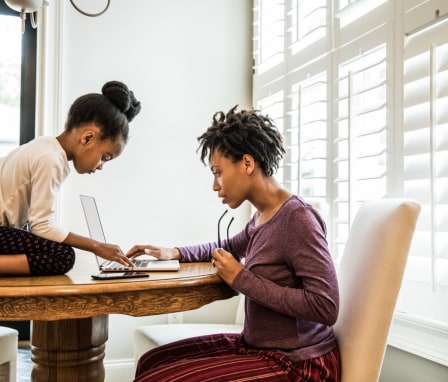 Woman working on laptop, young girl sitting on table in front of her