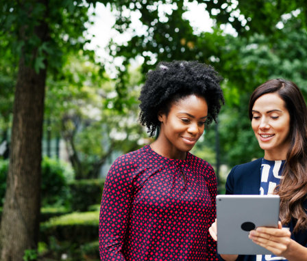 Two professional women looking at a tablet outside, surrounded by trees