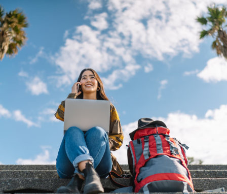 Woman talking on phone while on laptop, outside around palm trees