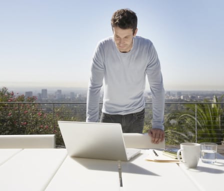 Man working on laptop on balcony with Los Angeles skyline in background