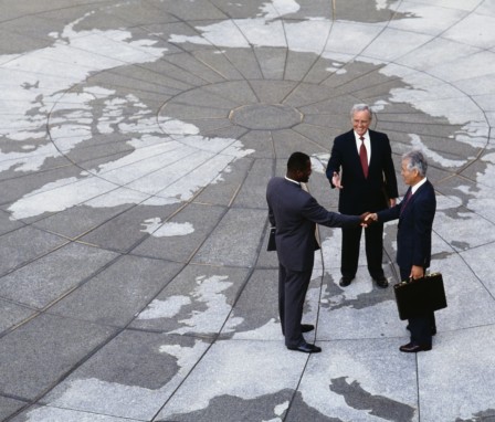 Three business men shaking hands, standing on concrete printed like a globe