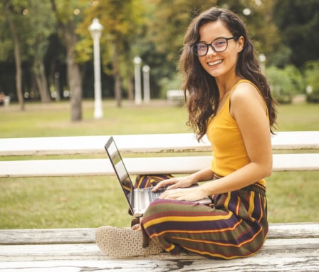 Young woman using laptop outside on park bench