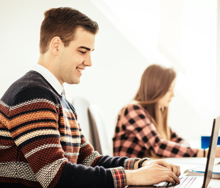 Male student smiling while working on laptop