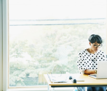 Woman working in office on laptop in front of big window