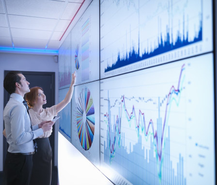 Two colleagues looking at multiple screens showing different types of charts and graphs