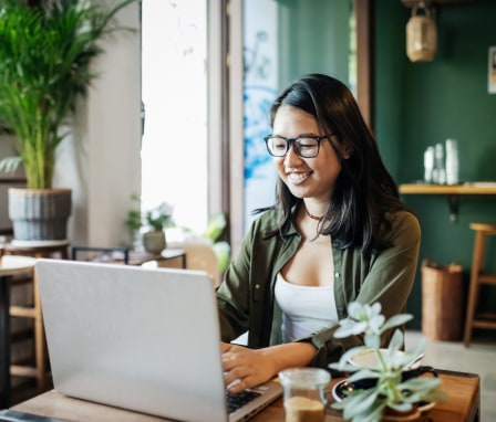 Woman smiling and typing on laptop in a cafe