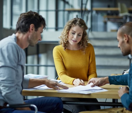 Three people discussing papers on a table
