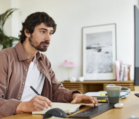 Man sitting at a desktop computer and writing in a notebook