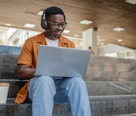 Online male student on a laptop sitting on stairs