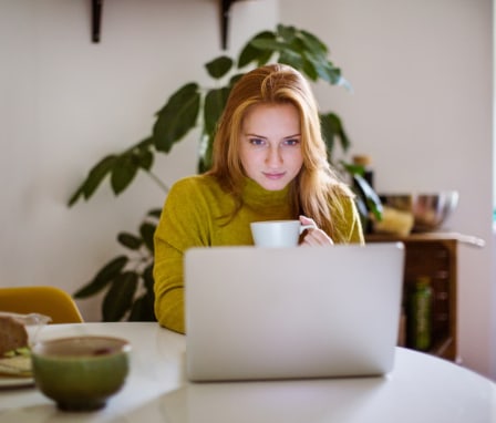 Woman reading on a laptop while drinking cofee