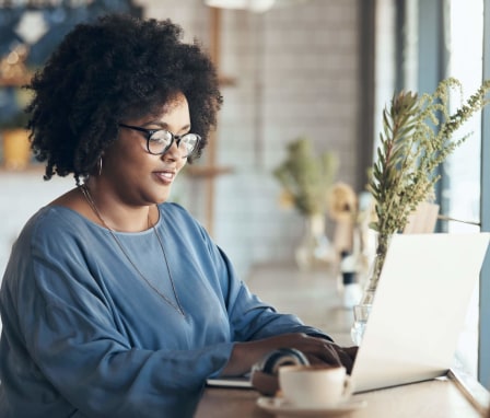 Young African-American female sitting and working on her laptop in a coffee shop during the day.