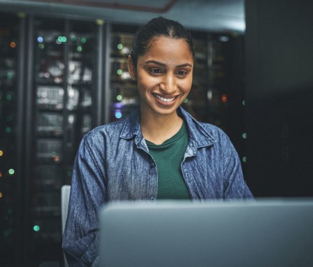 Person smiling at laptop around servers