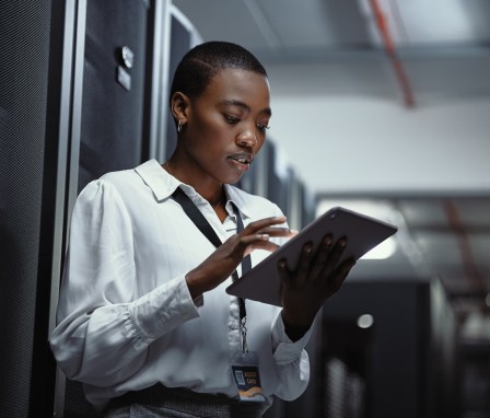 IT technician using a digital tablet in a server room. Female programmer fixing a computer system and network while doing maintenance in a datacenter. Engineer updating security software on a machine