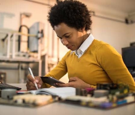 Person writing in notebook in front of desktop computer