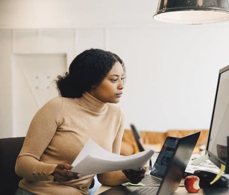 Woman holding papers and looking at computer