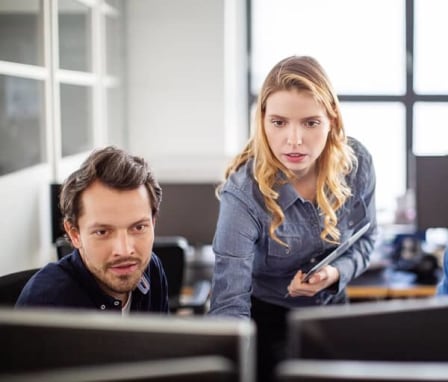 Woman helping two male colleagues on computers