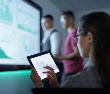 Woman using tablet to display charts on a screen to colleagues