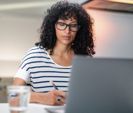 Woman taking notes while looking at laptop