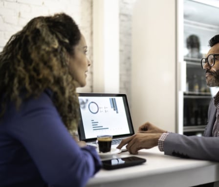 Two professionals talking beside laptop with graphs on the screen