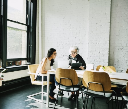 Two people talking at a table with laptops