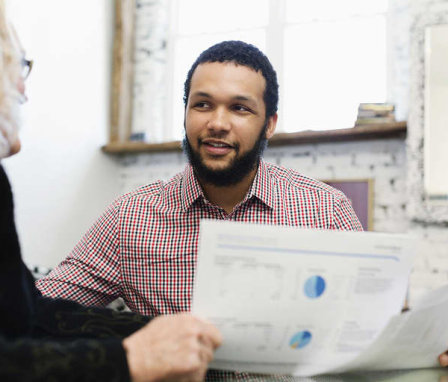 Two men talking in office about a paper with charts on it