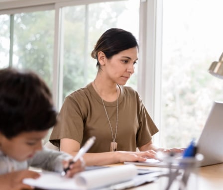 Veteran woman on a laptop at home beside kid