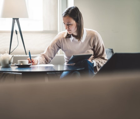 Woman writing and holding tablet beside lamp