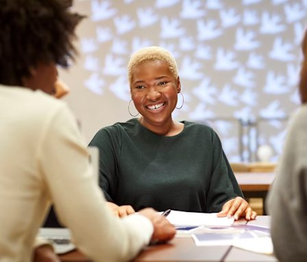 Person smiling at two others in a meeting, with papers laid out on the table in front of them