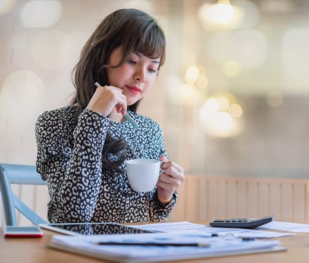 Woman drinking coffee while reading spreadsheets with a calculator